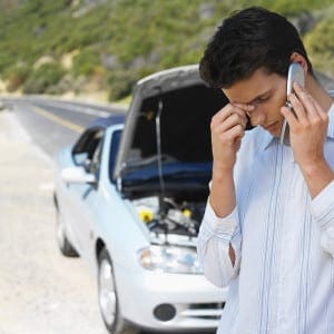 Close-up-of-young-man-talking-on-mobile-phone-with-car-bonnet-open